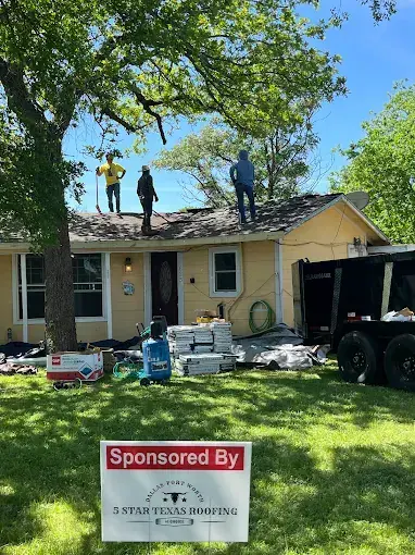 Roofing crew on a yellow house. Materials and truck parked in the yard. Sign reads "Sponsored By Star Texas Roofing".