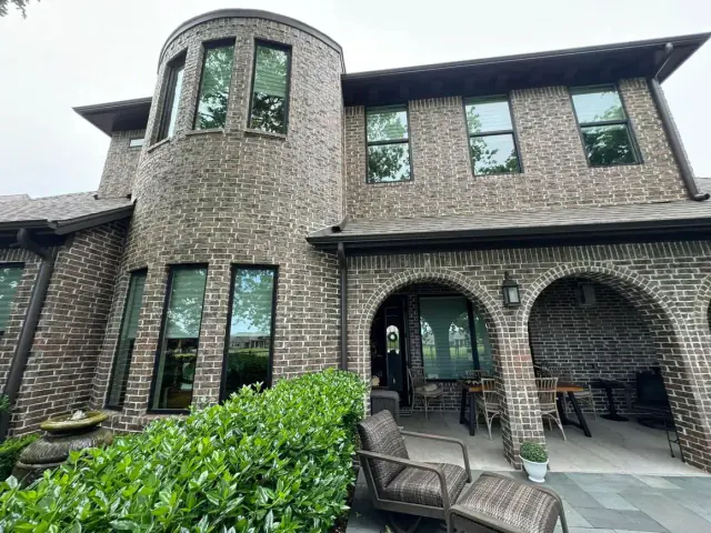 Brick house with tower and arched porch, greenery in foreground.