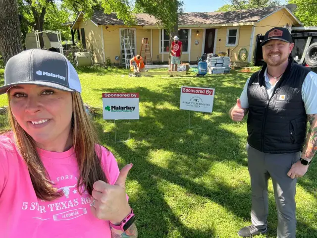 Two people giving thumbs up in front of a house under renovation, with construction workers visible in the background.