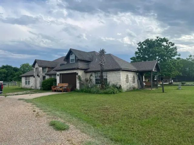 Stone house with multiple rooflines on grassy property under cloudy sky.
