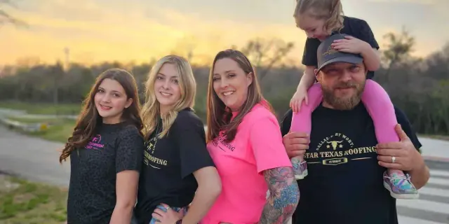 Family of five poses outdoors at sunset; father has child on shoulders.