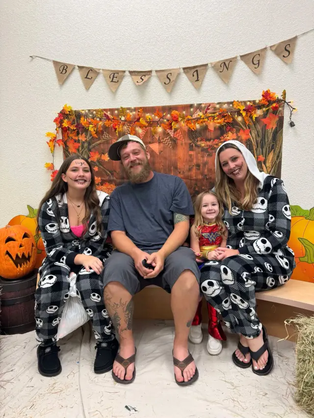 Family of four in Halloween pajamas seated in front of fall decorations.